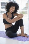Retrato de mulher sorridente em roupas esportivas sentado no tapete de exercício — Fotografia de Stock