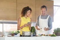 Пара готовит еду на кухне с цифровым планшетом — стоковое фото