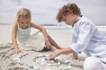 Братья и сестры играют с галькой на морском пляже — стоковое фото