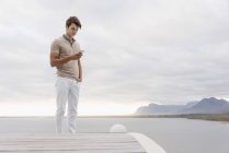 Hombre joven usando teléfono inteligente en la orilla bajo el cielo nublado - foto de stock
