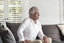 Задумчивый пожилой человек сидит дома на диване — стоковое фото