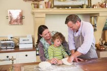 Милый маленький мальчик и его родители смешивают тесто на кухне — стоковое фото