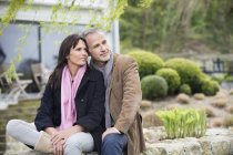 Romantic thoughtful couple sitting in garden and looking away — Stock Photo