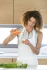 Woman pouring vegetable juice into glass in kitchen — Stock Photo