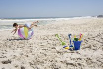 Маленький хлопчик балансує на барвистому м'ячі на піщаному пляжі — стокове фото