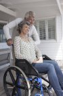 Happy senior man assisting wife in wheelchair on porch — Stock Photo