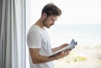 Junger Mann liest Zeitschrift gegen Glasscheibe — Stockfoto