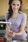 Sorrindo jovem mulher lavando tomates na cozinha e olhando para a câmera — Fotografia de Stock