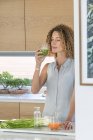 Mulher bebendo suco de legumes na cozinha — Fotografia de Stock