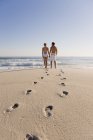 Footprints on sandy beach with couple standing on background and looking at view — Stock Photo