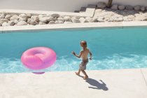 Boy playing with pink inflatable ring at poolside in summer — Stock Photo