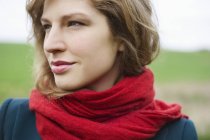 Молодая женщина в красном шарфе мечтает в поле — стоковое фото