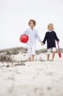 Siblings holding hands and walking on sandy beach — Stock Photo