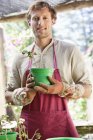 Uomo in grembiule piantare fiori in vaso all'aperto — Foto stock