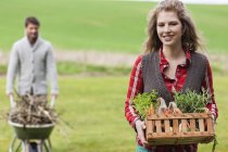 Woman holding basket of vegetables with husband collecting firewood in countryside — Stock Photo
