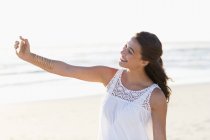 Щаслива молода жінка бере селфі зі смартфоном на пляжі — стокове фото