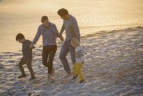 Bonne famille marchant sur la plage au coucher du soleil — Photo de stock