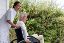 Enfermera asistiendo a hombre mayor en silla de ruedas en porche - foto de stock