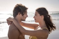 Sonriente pareja joven abrazándose en la playa soleada - foto de stock