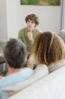Boy talking to parents while sitting on sofa in living room at home — Stock Photo
