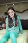 Portrait of smiling teenage girl sitting on bed — Stock Photo