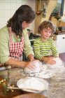 Grandmother and little boy kneading dough at kitchen — Stock Photo
