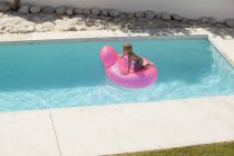 Menino que joga no anel inflável rosa na piscina — Fotografia de Stock
