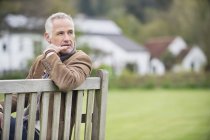 Вдумчивый взрослый мужчина сидит на скамейке в парке — стоковое фото