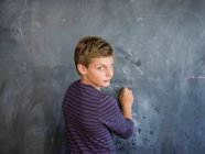 Junge schreibt in einem Klassenzimmer an eine Tafel — Stockfoto