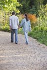 Задний вид на зрелую пару, гуляющую в солнечном саду — стоковое фото