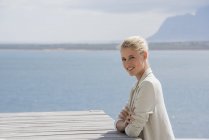 Ritratto di giovane donna sorridente ed elegante seduta a tavola sulla riva del lago — Foto stock