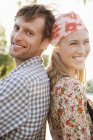 Side view of smiling couple standing back to back and looking at camera — Stock Photo