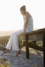 Pensive elegant woman sitting on a boardwalk on coast — Stock Photo