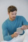Junger Mann fährt mit digitalem Tablet gegen graue Wand — Stockfoto