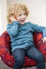 Cute boy with blonde hair talking on a mobile phone in armchair — Stock Photo