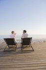 Couple sitting on deck chairs on beach and talking — Stock Photo