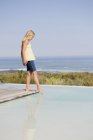 Маленька блондинка стоїть на платформі в нескінченному басейні на морському узбережжі — стокове фото