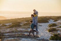 Jovem família feliz andando na praia ao pôr do sol — Fotografia de Stock