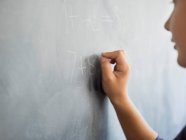 Gros plan d'un garçon écrivant sur un tableau noir dans une salle de classe — Photo de stock