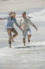 Anziani coppia scherzare sulla spiaggia e tenersi per mano — Foto stock