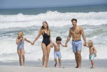 Familia feliz caminando por la playa tomados de la mano - foto de stock