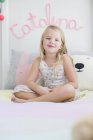 Portrait of happy little girl sitting on bed with legs crossed — Stock Photo