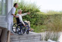 Infermiera femminile che assiste l'uomo anziano in sedia a rotelle sul portico — Foto stock