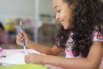 Щаслива маленька дівчинка робить домашнє завдання вдома — стокове фото