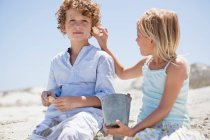 Девушка держит скорлупу на ухе своего брата на пляже — стоковое фото