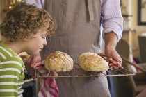 Lindo niño oliendo pan recién horneado en manos masculinas - foto de stock
