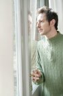 Man in pullover looking out through door glass — Stock Photo