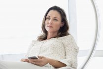 Mature woman relaxing in glass chair with mobile phone — Stock Photo