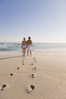 Pegadas na praia de areia com casal em pé no fundo e olhando para a vista — Fotografia de Stock
