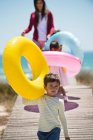 Crianças com sua mãe segurando anéis infláveis em um calçadão na praia — Fotografia de Stock